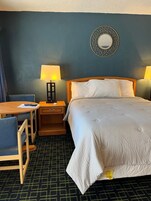 Habitación de hotel con una cama, dos lámparas de noche, una mesita con una silla y un espejo adosado a la pared.