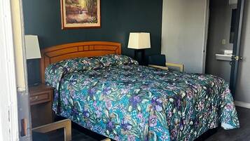 A bedroom with a wooden bed, a nightstand, a lamp, a chair, and a painting on the wall.
