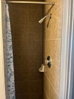 Zona de ducha con azulejos marrones, ducha y cortina con estampado floral.