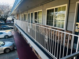 Un hotel con balcón cubierto, varias ventanas y un estacionamiento con coches.