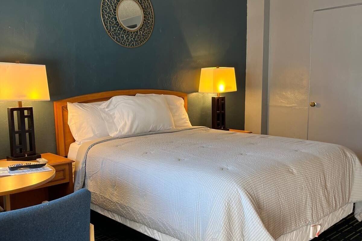 Una habitación de hotel con una cama, dos lámparas de noche, un espejo redondo, un escritorio con una silla y una puerta.