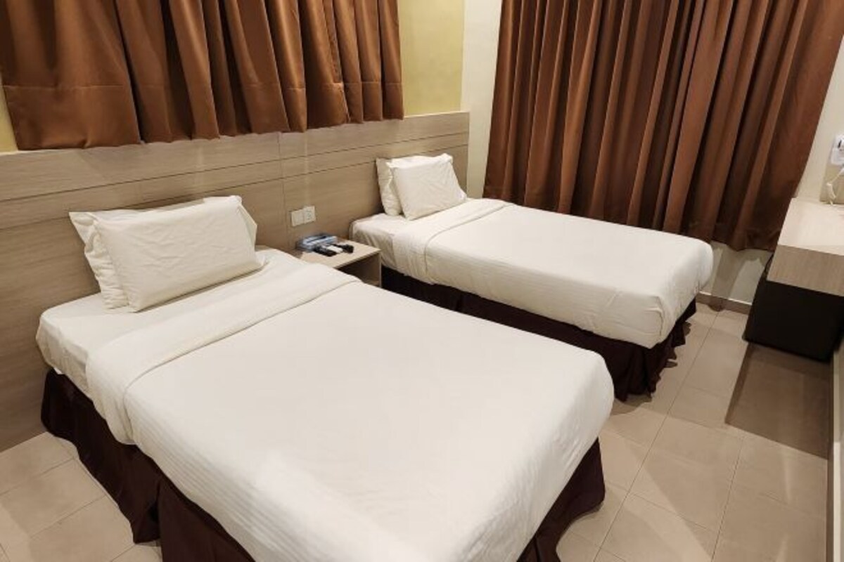 A hotel room with two single beds, a bedside table, a nightstand, and a bathroom area.