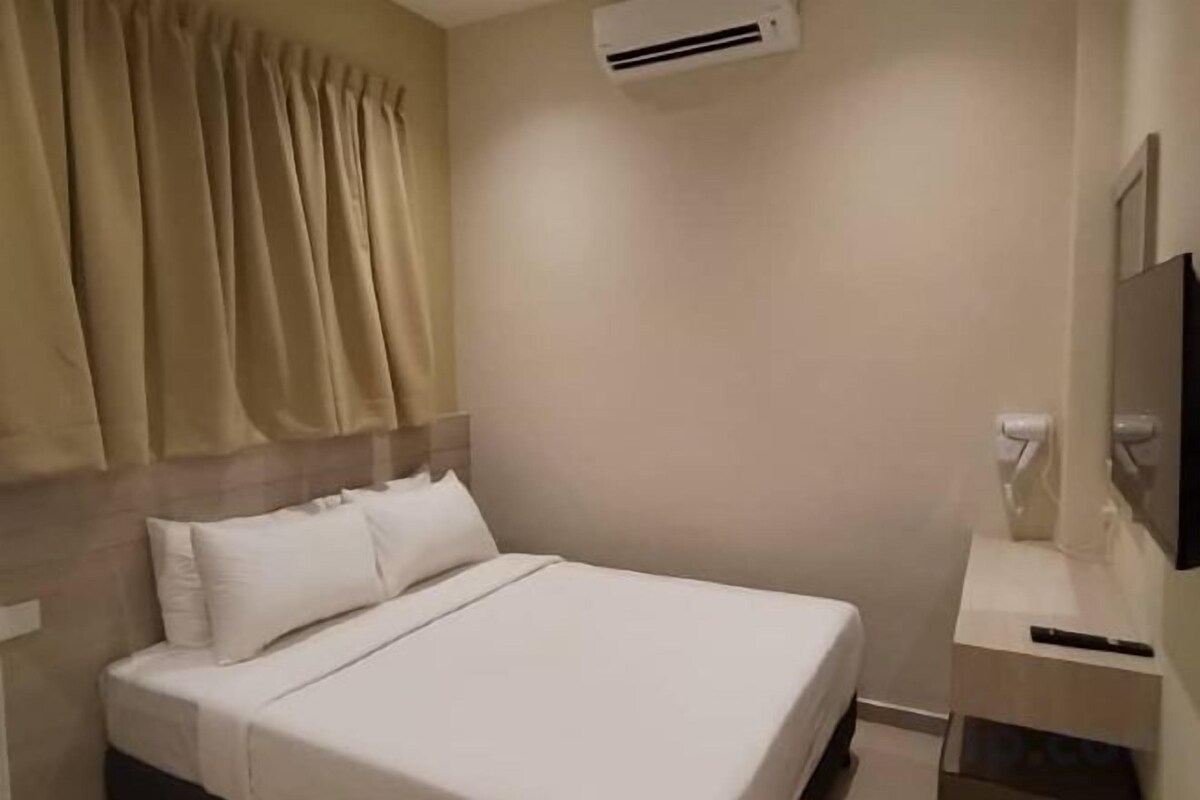 A hotel room with a bed, a bedside table, a TV, and an air conditioning unit.