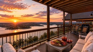 Una terraza de madera con asientos al aire libre, una mesa con una tabla de quesos y una vista del lago al atardecer.