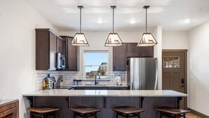 Una cocina moderna con armarios de madera oscura, una isla grande con taburetes de bar, electrodomésticos de acero inoxidable e iluminación colgante.