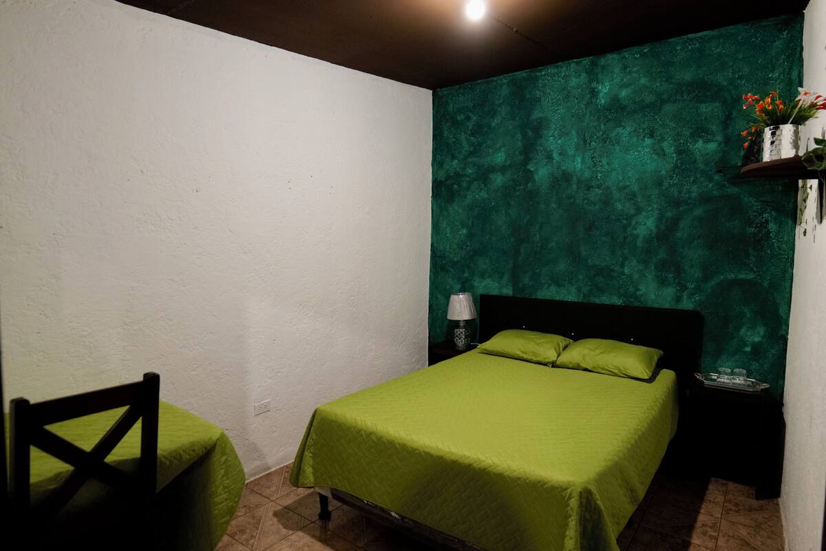 Ein Schlafzimmer mit einer grünen Bettdecke, einem Nachttisch mit Lampe und einer Wand mit strukturierter grüner Farbe.