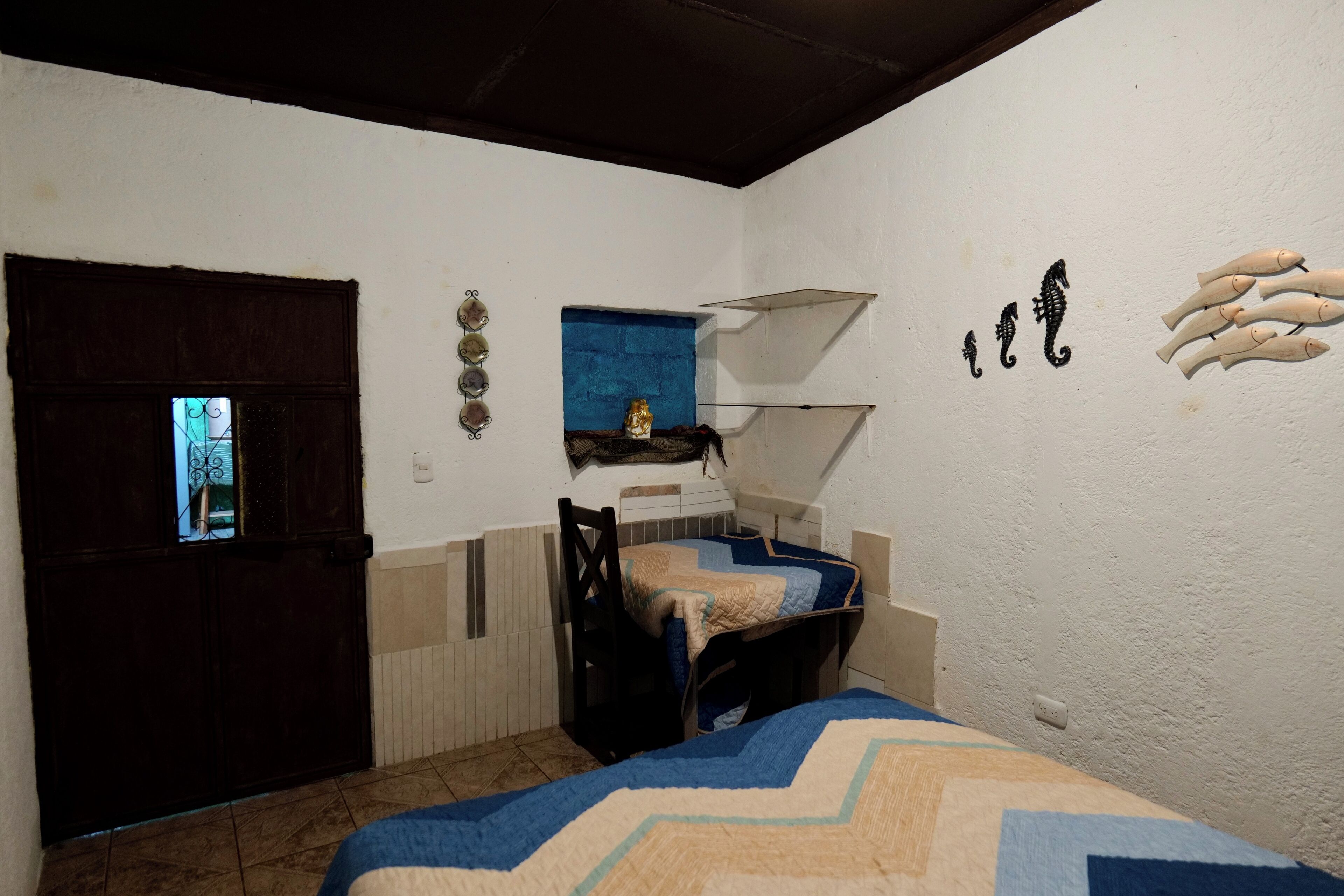 A small room with a bed, a chair, a window with a view, and a shelf with decorative items.