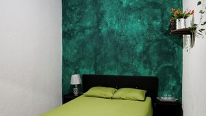 A bedroom with a green bedspread, a nightstand with a lamp, and a teal textured wall. - Wonderland Hostel (Antigua Guatemala)
