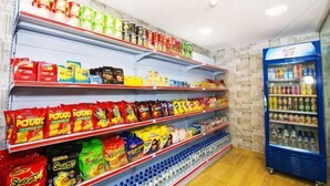Un supermercado con estantes llenos de diversos productos, un expositor refrigerado y una máquina expendedora azul.