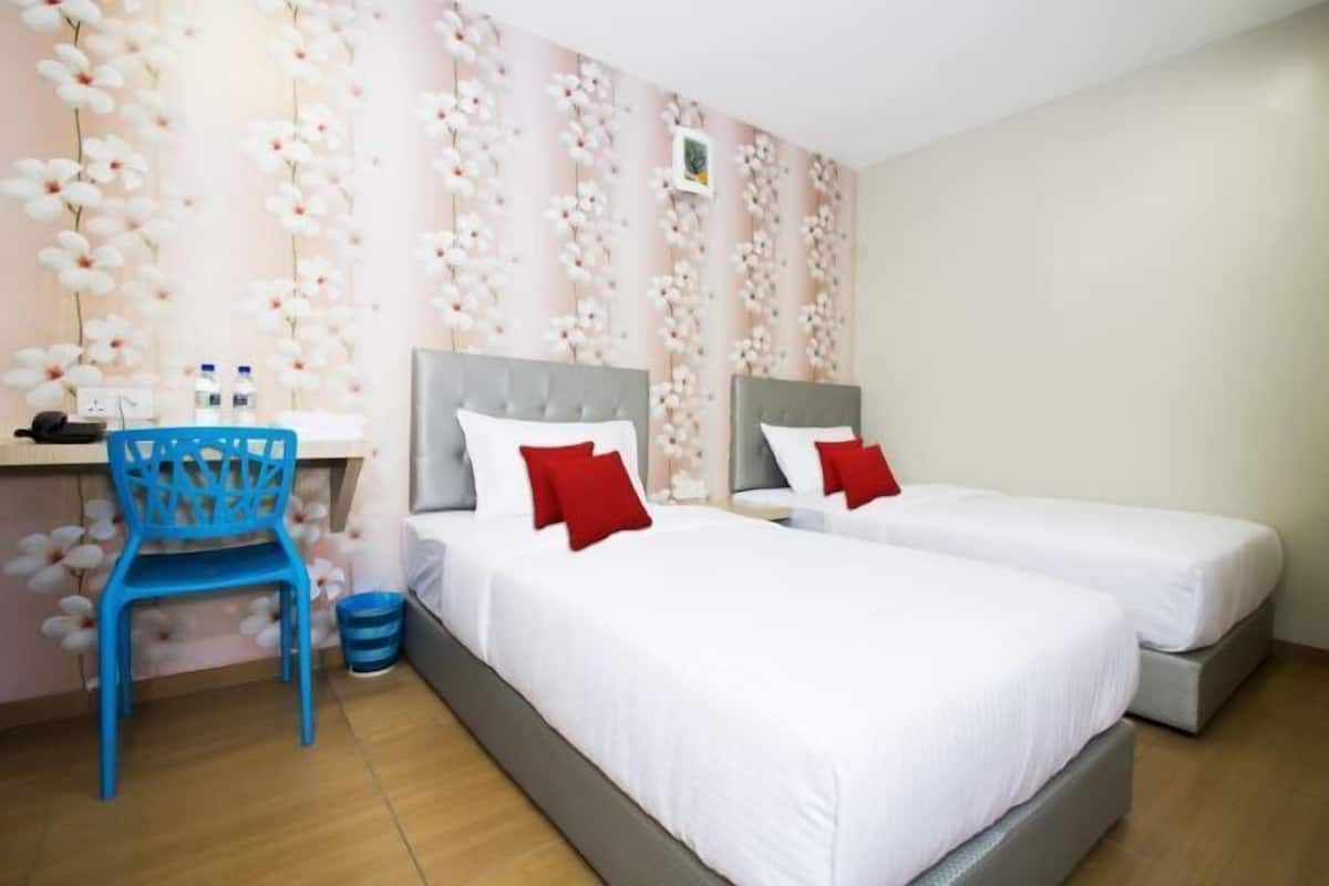 A hotel room with two beds, a desk, a chair, and a wall with a floral pattern.