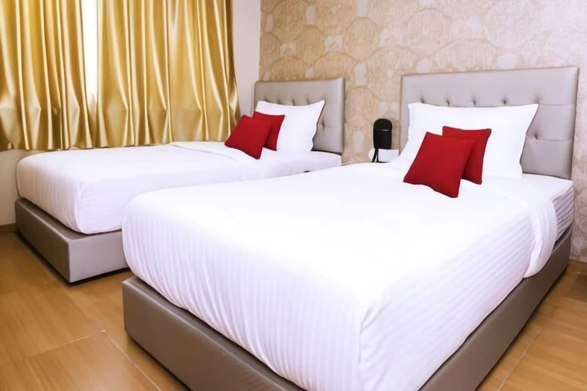 Two twin beds with white bedding and red pillows, a telephone, and a patterned wall.