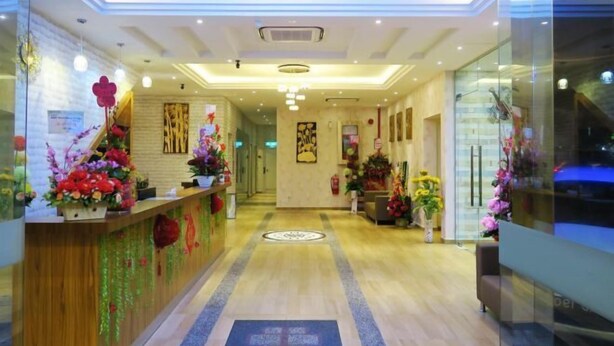Zona de recepción de un hotel con un mostrador de madera, una lámpara de araña en el centro y decoración floral.