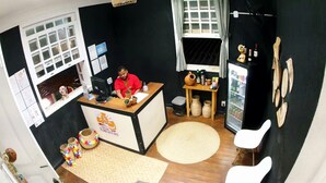 Ein Zimmer mit einer Rezeption, einem Computer, einem kleinen Tisch mit Pflanze, einem Kühlschrank und einem großen Wollteppich.