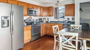 A modern kitchen with wooden cabinets, stainless steel appliances, and a dining area with white chairs. - Rainbow Ranch: Family Friendly 4 Bedroom in Lovely Williamstown, 5 min to ARK! (Williamstown)