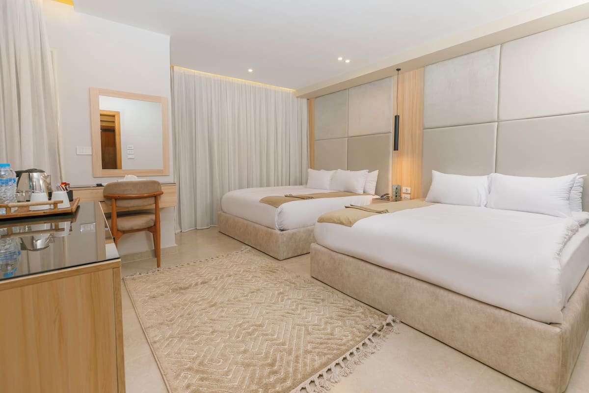 A hotel room with two beds, a desk, a chair, a mirror, and a large window with curtains.