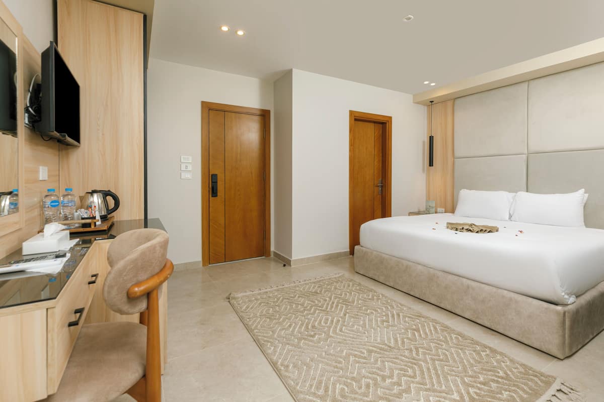 A modern hotel room with a bed, a desk with a chair, a television, and a door.