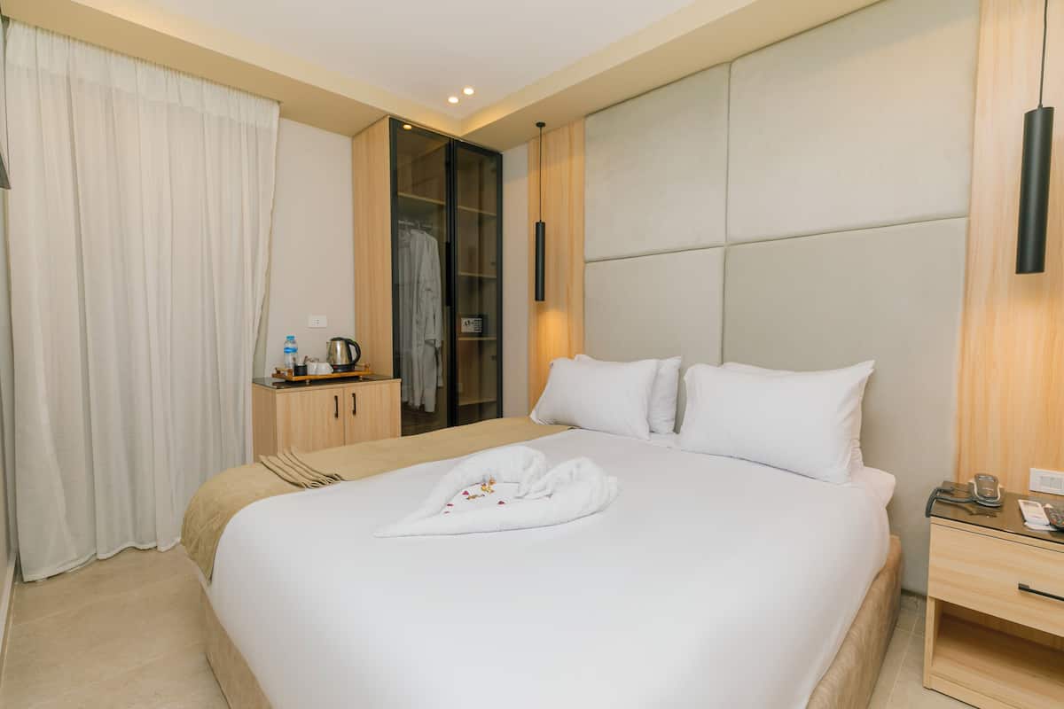 A hotel room with a large bed, a wooden nightstand, a wardrobe, and a bathroom with a shower curtain.