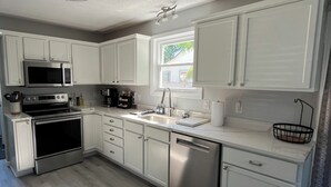 A modern kitchen with white cabinetry, stainless steel appliances, and a window providing natural light. - Lakeside Horizon - minutes to Lake Michigan Pere Marquette Beach & Muskegon Lake (Muskegon)