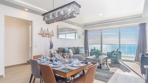 Ein modernes Wohnzimmer mit Essbereich, großen Fenstern und Blick auf den Ozean.