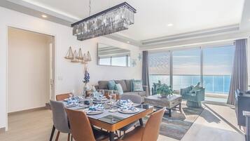 A modern living room with a dining area, large windows, and a view of the ocean.
