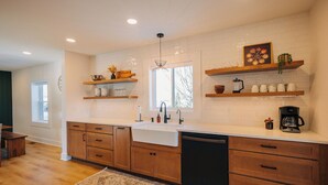Una cocina con armarios de madera, encimera blanca, un lavabo y una cafetera.