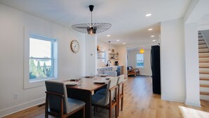 Una cocina moderna con armarios blancos, un refrigerador negro y una zona de comedor con mesa y sillas de madera.