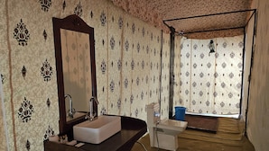 Ein Badezimmer mit einem Holzbadezimmer-Möbelstück, einem Spiegel, einem Waschbecken und einer Toilette. Die Wände sind mit einem gemusterten Tapeten versehen, und es gibt ein Fenster mit Blick nach außen.
