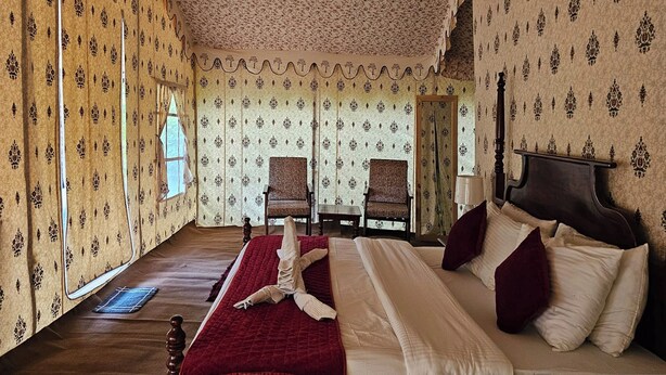 Ein Zimmer mit gemustertem Wandpapier, einem großen Bett mit roter und weißer Bettwäsche, zwei Stühlen, einem Holzboden und einem Spiegel an der Wand.