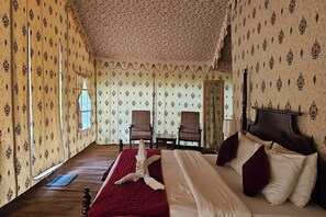 Ein Zimmer mit gemustertem Wandpapier, einem großen Bett mit roter und weißer Bettwäsche, zwei Stühlen, einem Holzboden und einem Spiegel an der Wand.