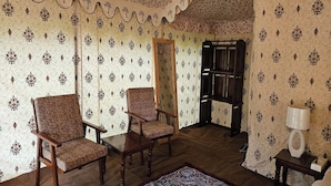 Ein Zimmer mit strukturierter Tapete, zwei Sessel, ein Tisch, ein Spiegel, eine Kommode und eine Lampe.