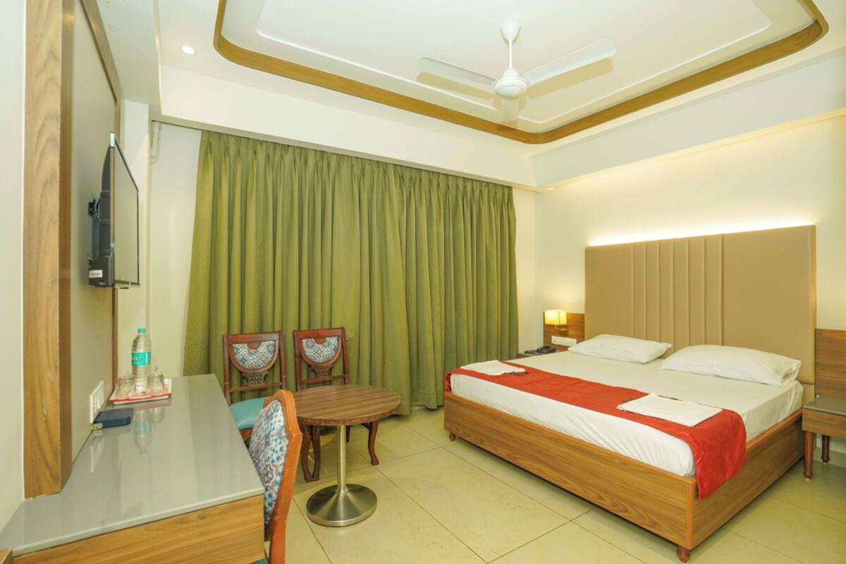 A hotel room with a bed, a desk, a chair, a television, and a ceiling fan.