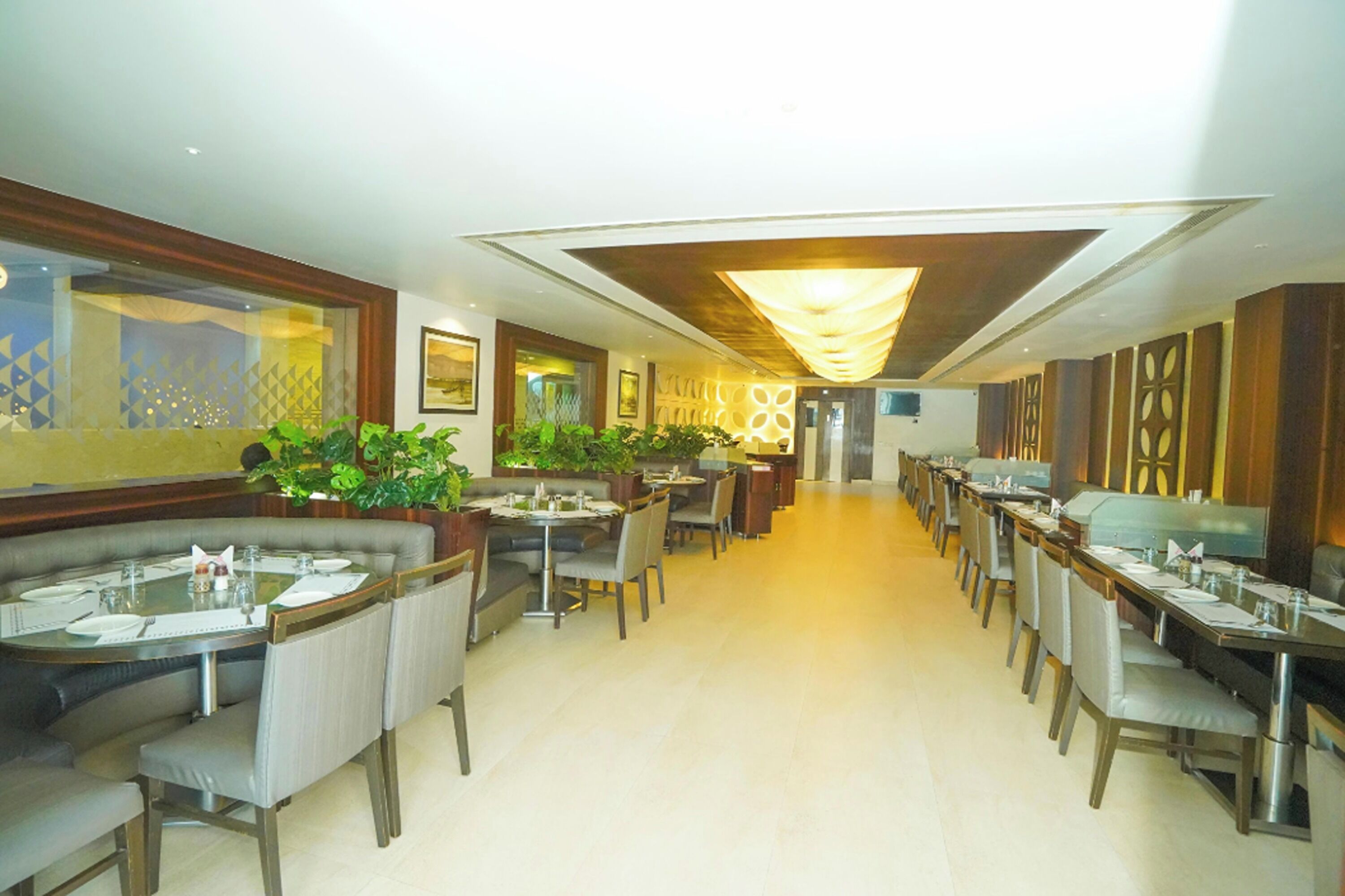 Un restaurante amplio con varias mesas y sillas para comer, un candelabro decorativo en el centro y plantas en macetas.