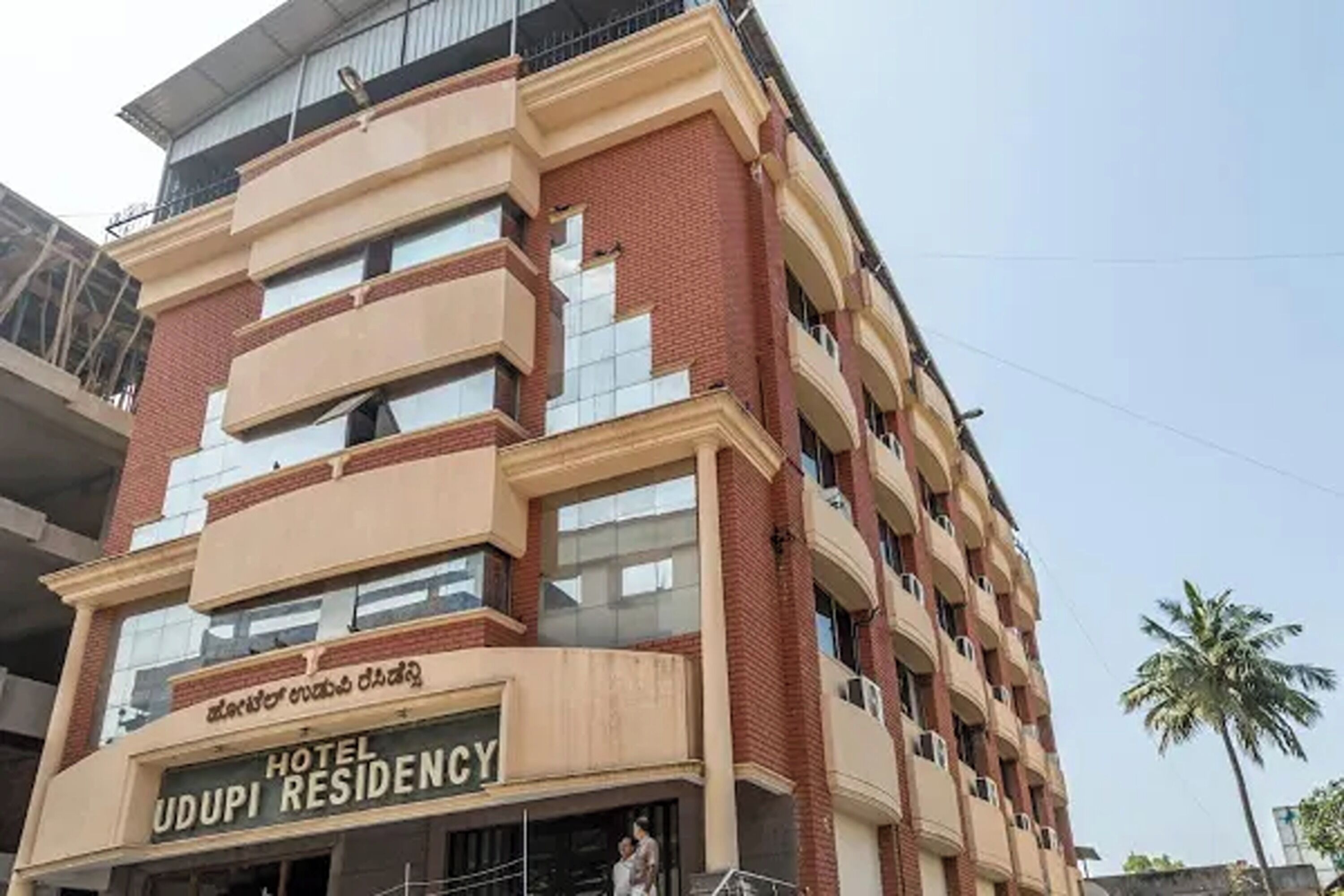 Un hotel de varios pisos con un cartel llamativo que dice 'HOTEL UDUPI RESIDENCY'.