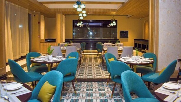 Un comedor con mesas redondas y sillas color turquesa, un suelo estampado y una araña.