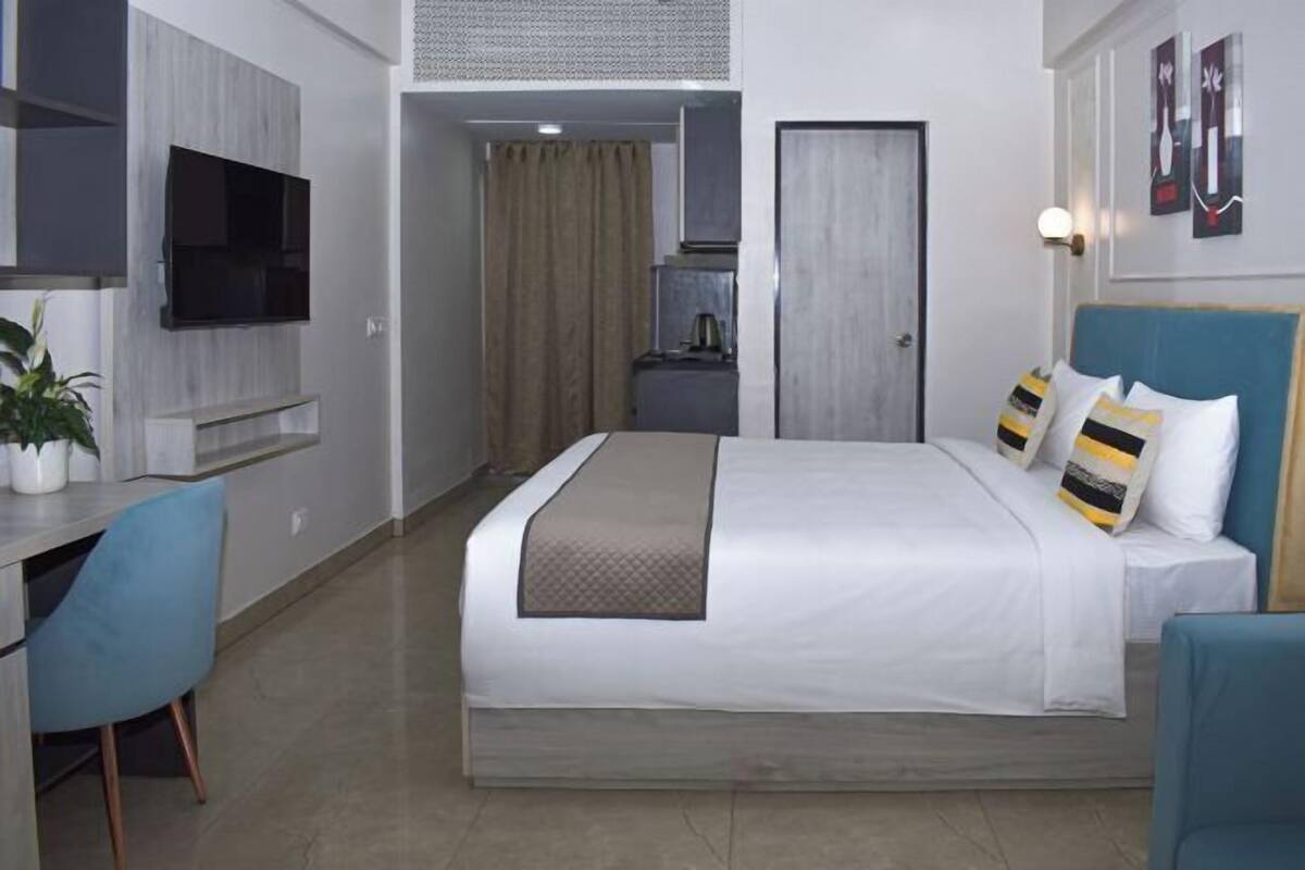 A hotel room with a bed, desk, chair, TV, and artwork on the walls.