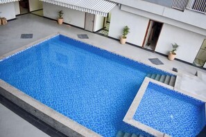 Une piscine rectangulaire dont le bord est recouvert de carreaux, entourée d’une terrasse en béton et de plantes en pot.
