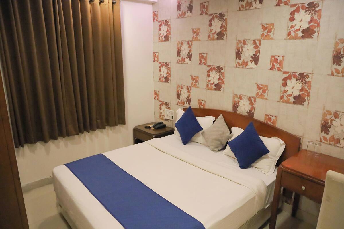 A hotel room with a bed, a nightstand, a chair, and a window with curtains.