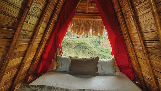 Una habitación acogedora de techo triangular con una cama en el centro, almohadas y una toalla doblada con cuidado.