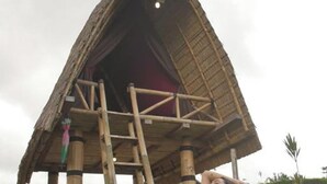 Una persona realizando una postura de yoga sobre una esterilla frente a una construcción con techo de paja.