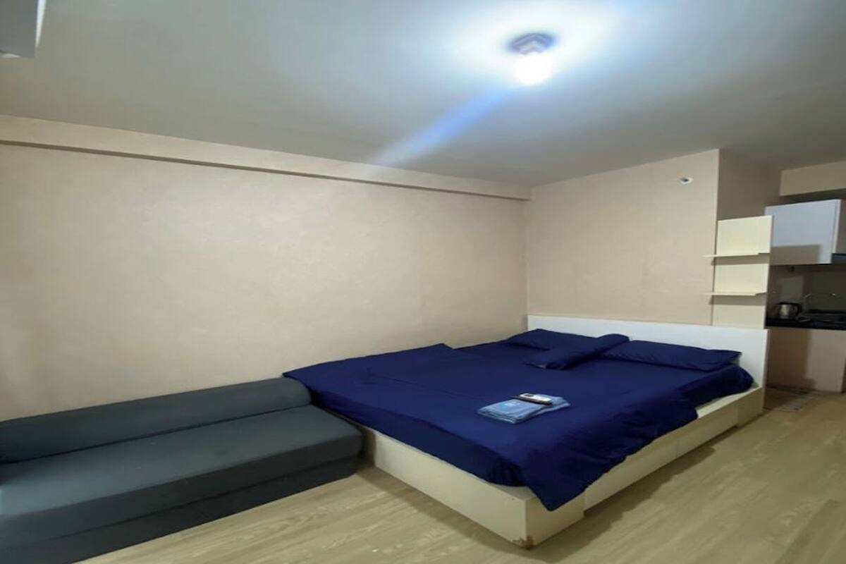 A small, modern room with a single bed, a bench, and a kitchenette area.