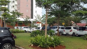 A parking lot with several cars parked, surrounded by greenery and a building in the background. - Jasmine Park Jp Rooms (Dramaga)