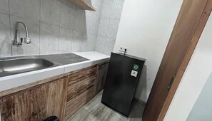 Μια μικρή, λειτουργική κουζίνα με νεροχύτη, ένα μικρό ψυγείο και ξύλινα ντουλάπια.