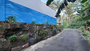 A narrow road flanked by a decorative wall with a painted mural of clouds and trees. - Maisaba Living Sibang Gede (Abiansemal)