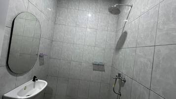 Un baño con espejo, lavabo, ducha y paredes con azulejos.