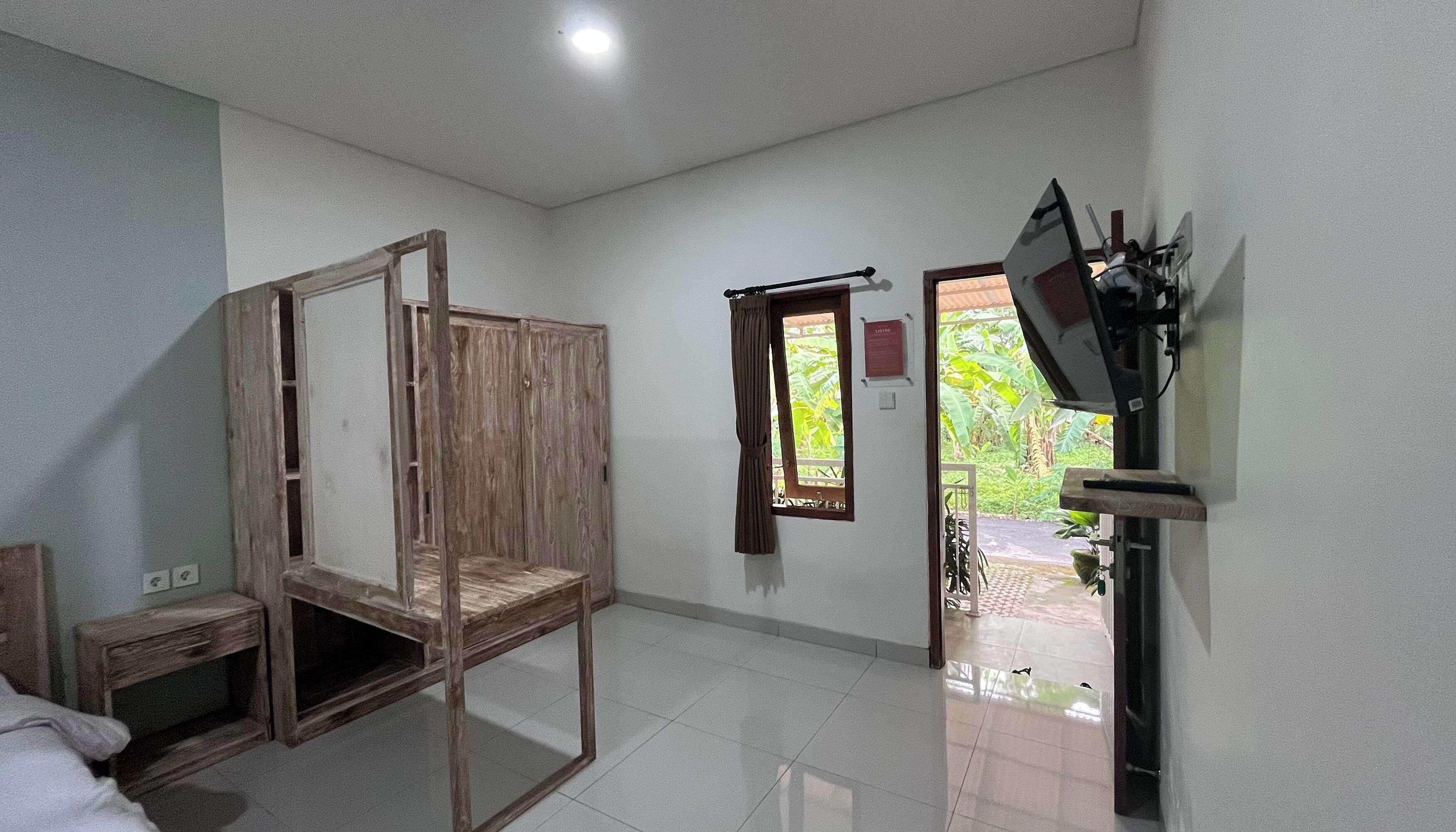 Quarto com estrutura de cama de madeira, mesa de cabeceira pequena, TV fixada na parede e janela com cortinas.