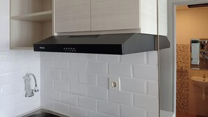 A kitchen with white tiled backsplash, a black range hood, and a light wooden cabinet above the range.