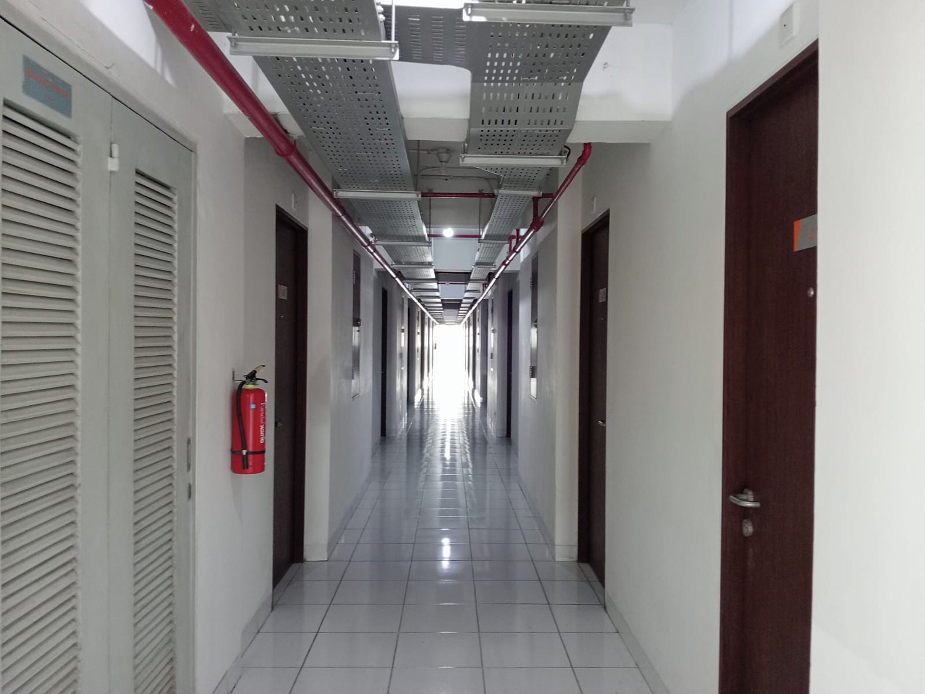 A long, narrow hallway with white tiled floors and doors on both sides.
