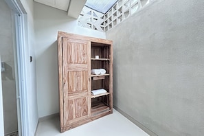 A wooden wardrobe with shelves, located in a corner of a room with a skylight above.