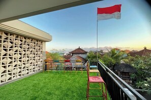 A balcony with a flag, a white lattice fence, and a view of houses and greenery. - Sekar Tunjung Guest House Seminyak Bali (Denpasar)
