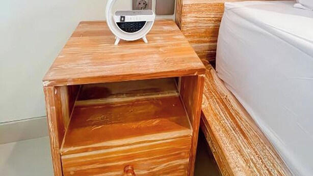 A wooden nightstand with a radio, a drawer, and a bed with white bedding. - Sekar Tunjung Guest House Seminyak Bali (Denpasar)